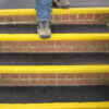 Booted feet walking down a set of stairs with anti slip stair treads
