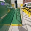 green access ramp with yellow and grey handrail going to a green building